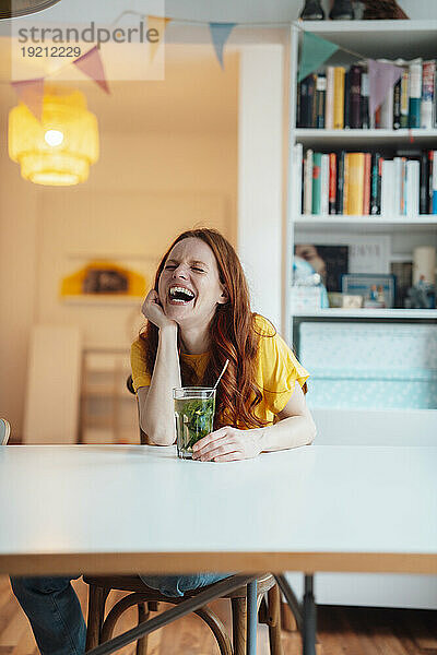 Fröhliche Frau sitzt zu Hause mit Glas