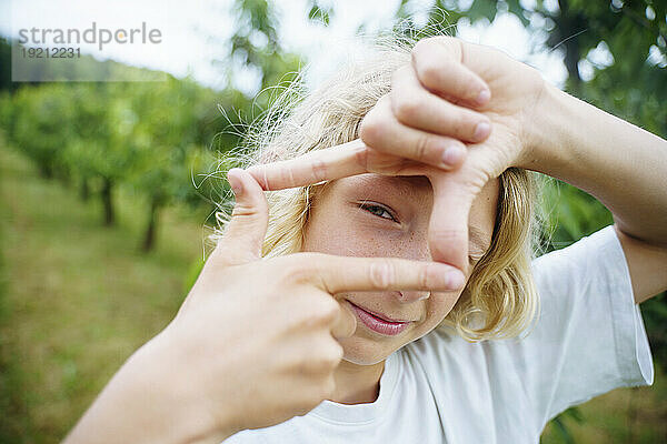 Blond boy showing finger frame sign in garden