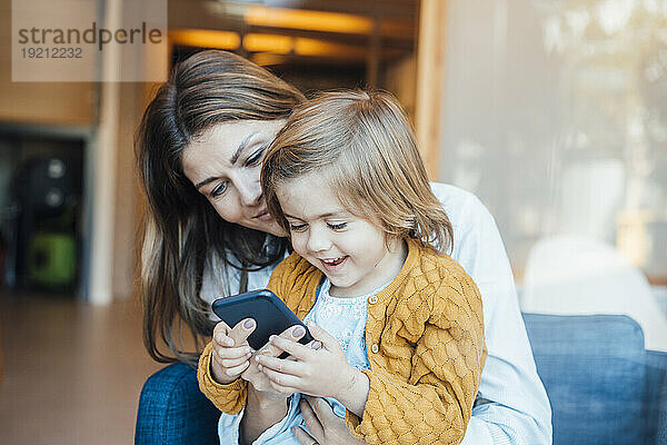 Glückliche Tochter nutzt Smartphone mit Mutter zu Hause