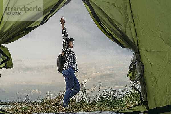 Lächelnde Frau mit erhobenem Arm steht vor dem Zelt unter freiem Himmel