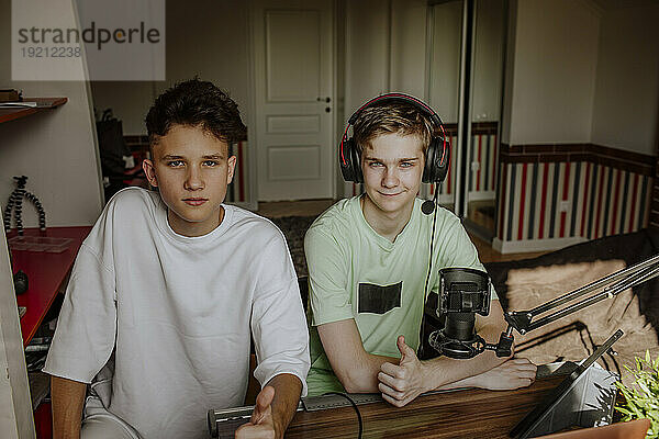 Teenage boys podcasting and showing thumbs up sign at home