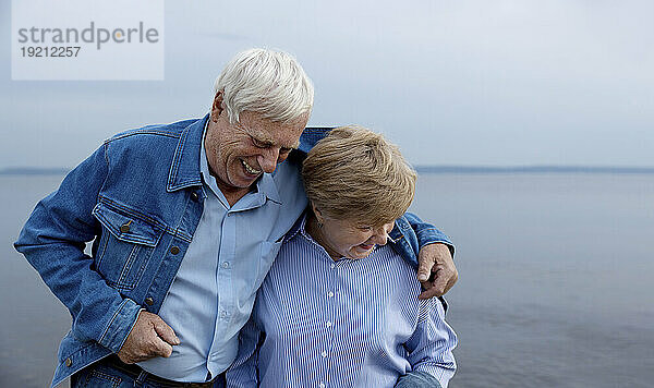 Älteres Paar lacht mit ausgestrecktem Arm am Strand