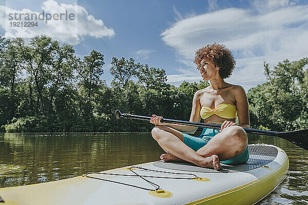 Junge Frau sitzt auf einem Paddleboard im See