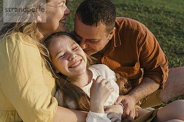 Lächelnde Eltern mit Tochter  die Spaß auf Gras haben