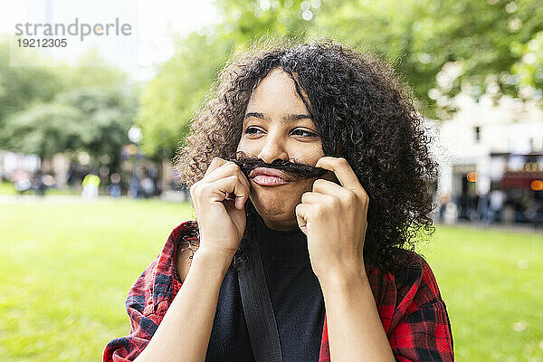 Playful woman making mustache with hair in park