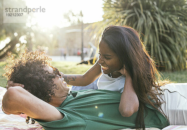 Smiling couple spending leisure time lying in park at sunny day