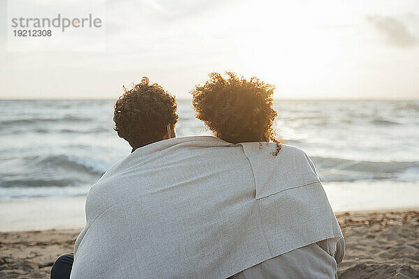 Paar sitzt zusammen vor dem Meer am Strand