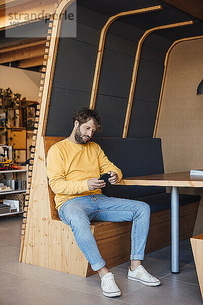 Geschäftsmann sitzt im Büro und benutzt Smartphone