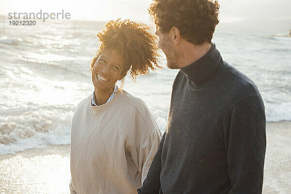 Glückliches Paar schaut sich an und geht an einem sonnigen Tag vor dem Meer spazieren