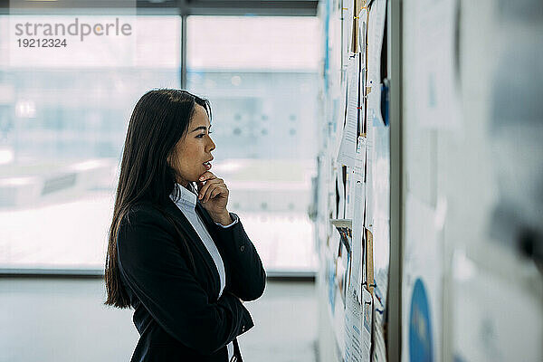 Thoughtful businesswoman examining bulletin board at office