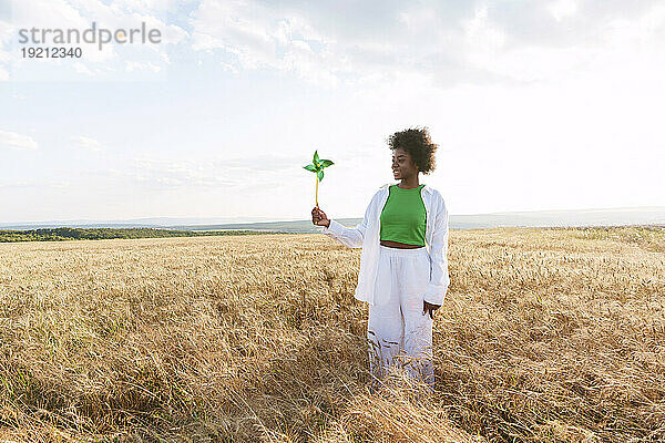 Junge Frau mit Windradspielzeug steht auf dem Feld
