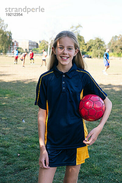 Glückliches Mädchen hält Sportball auf dem Fußballplatz
