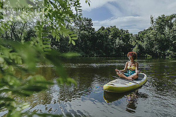 Woman meditating on paddleboard in lake