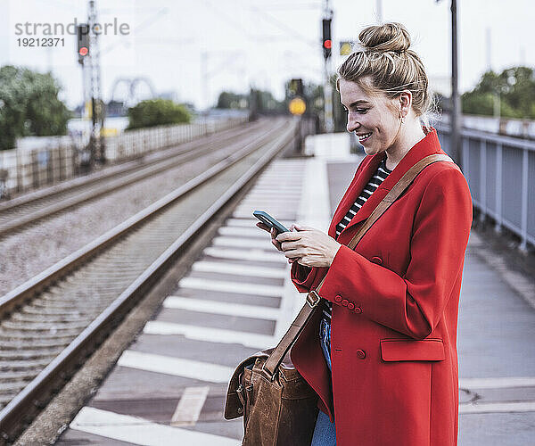 Glückliche Frau benutzt Smartphone am Bahnhof