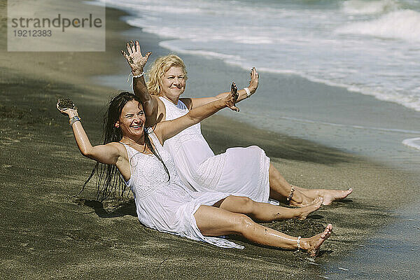 Sorglose Freunde spielen mit nassem Sand und sitzen am Strand