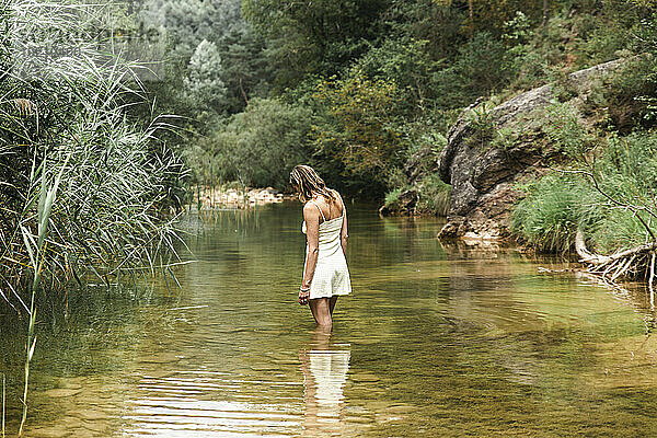 Frau steht im Fluss am Wald