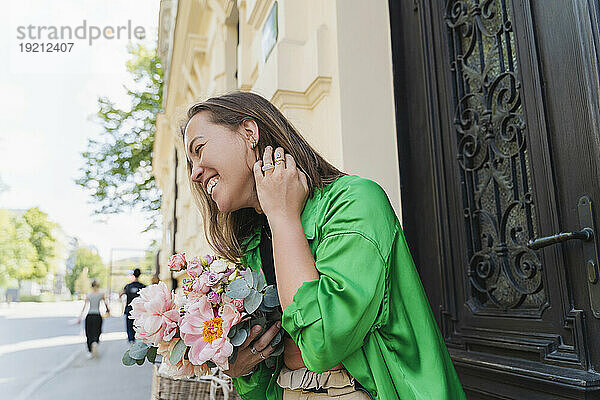 Glückliche Frau mit Blumenstrauß vor dem Gebäude