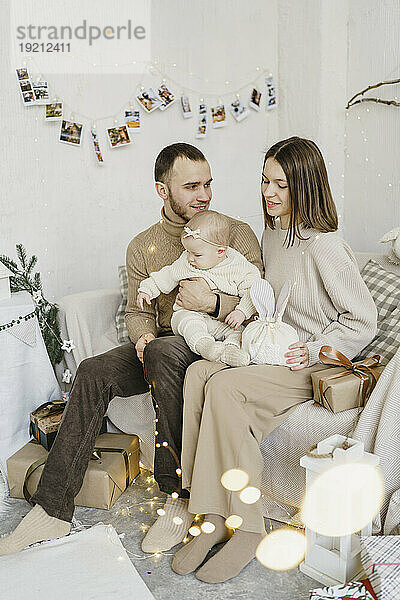Happy parents with baby daughter sitting on sofa at home