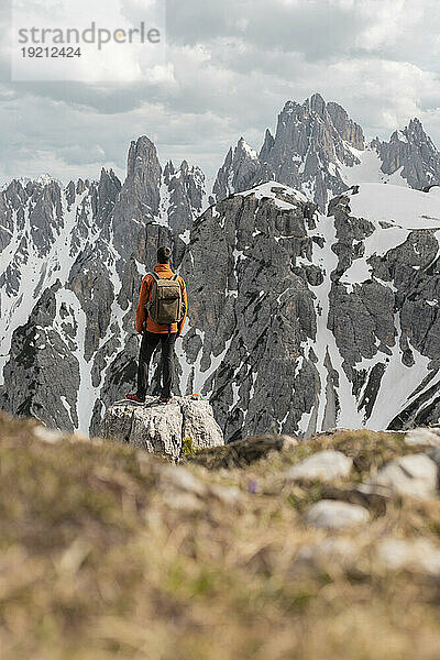 Junger Entdecker mit Rucksack blickt im Sommer auf schneebedeckte Berge