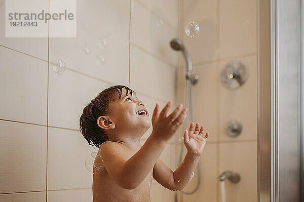 Happy boy playing with soap bubbles in bathroom