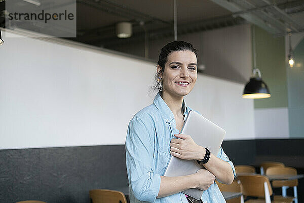 Lächelnder Freiberufler steht mit Laptop im Café