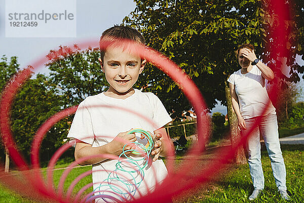 Junge hält Federspielzeug mit Mutter im Hintergrund im Park