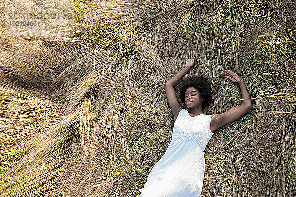 Junge Frau mit geschlossenen Augen entspannt sich auf trockenem Gras im Feld
