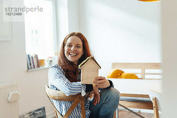 Happy redhead woman sitting with model house at home