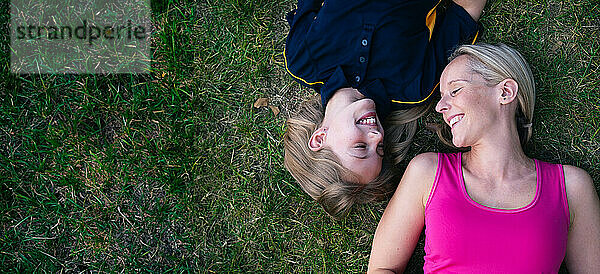 Smiling mother and daughter lying on grass in park