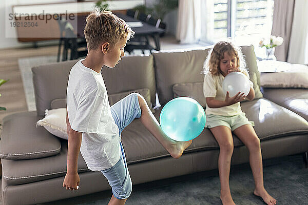 Siblings playing with balloons in living room at home
