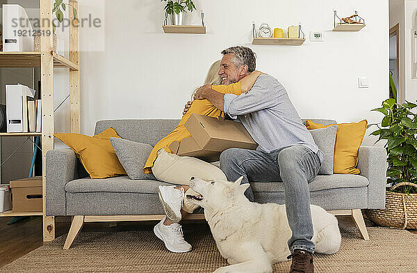 Glückliches Paar  das sich zu Hause umarmt und neben dem Hund auf dem Sofa sitzt