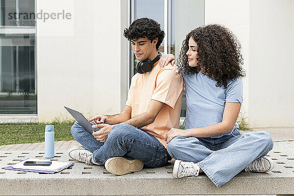 Student benutzt Laptop und erklärt Freund auf Betonbank auf dem Campus