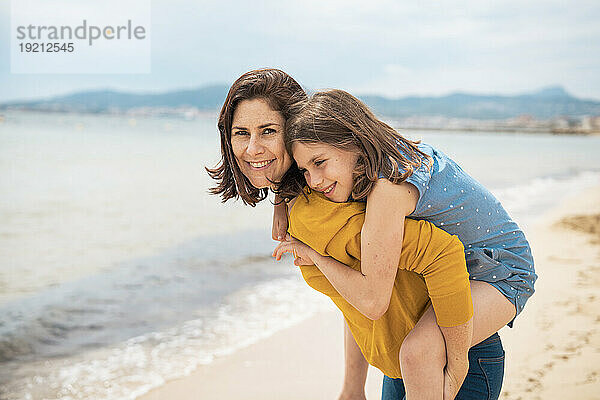 Lächelndes Mädchen genießt Huckepackfahrt am Strand