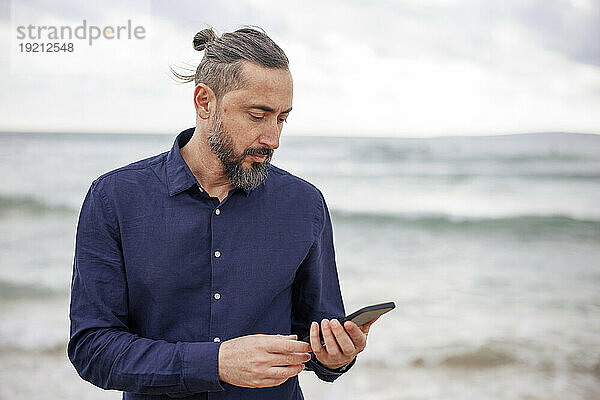 Reifer Mann benutzt Smartphone am Strand