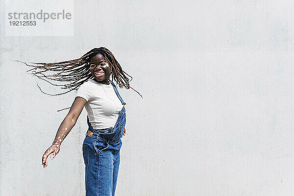 Happy young woman tossing hair and dancing in front of white wall