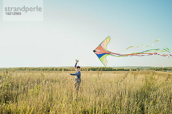 Happy boy flying kite and running in field under sky