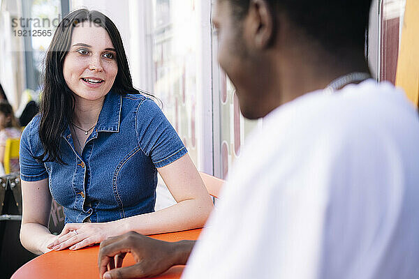 Lächelnde junge Frau im Gespräch mit Mann im Straßencafé