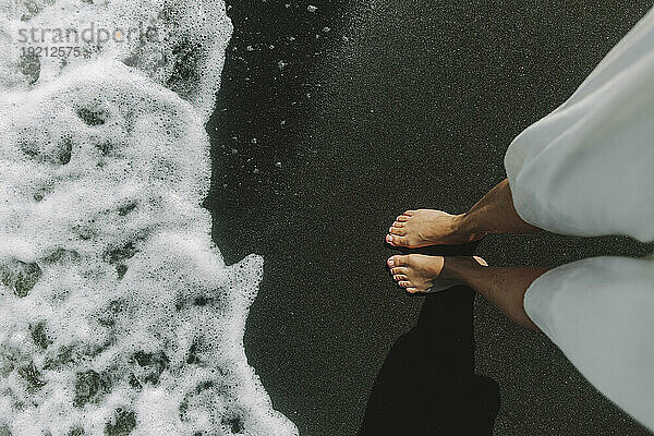 Frau steht auf schwarzem Sand in Ufernähe am Strand
