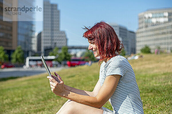 Lächelnde Frau mit Tablet-PC im Gras sitzend