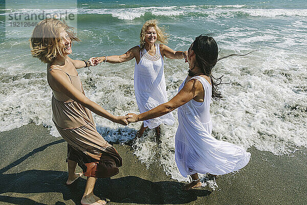 Fröhliche Freunde halten Händchen und spielen Ring um das rosige Meer am Strand