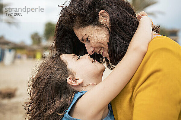 Glückliche Mutter umarmt ihre Tochter und hat Spaß mit ihr am Strand