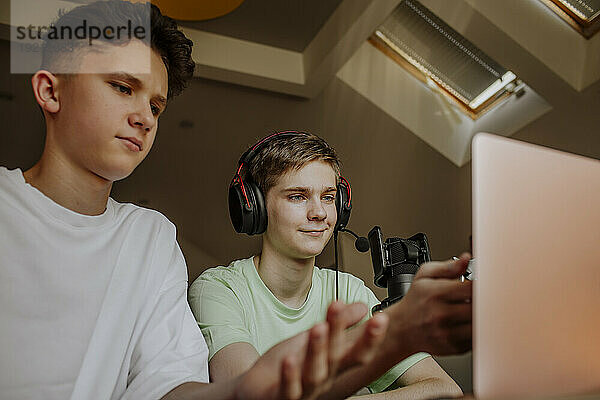 Teenage friends podcasting and gesturing in front of laptop