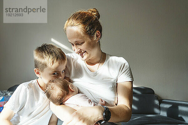 Mother breastfeeding newborn daughter near son at home