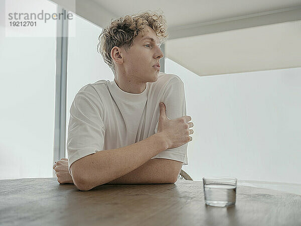 Nachdenklicher Mann sitzt mit einem Glas Wasser am Tisch zu Hause