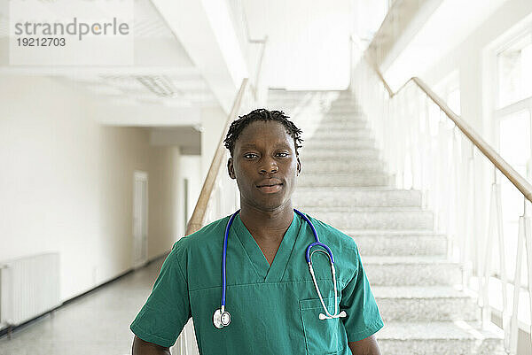Confident doctor with stethoscope in front of steps at hospital corridor
