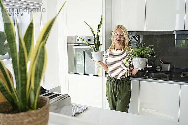 Happy woman standing with potted plants in kitchen at home