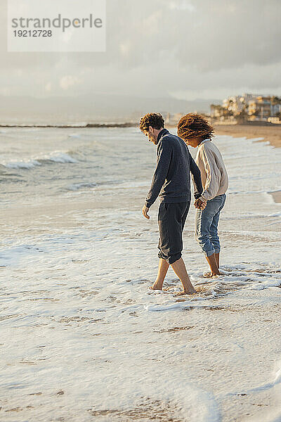 Couple holding hands and standing in water at beach