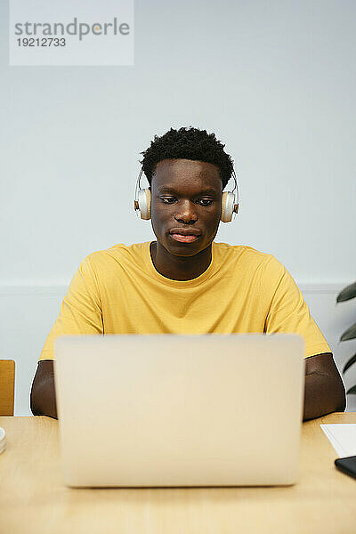 Student mit kabellosen Kopfhörern und Laptop am Schreibtisch