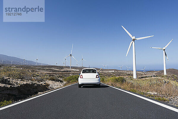 Auto bewegt sich auf der Straße inmitten von Windkraftanlagen unter blauem Himmel