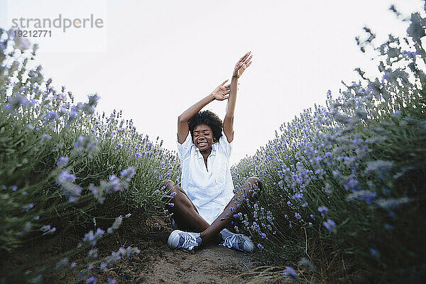 Young woman with arms raised sitting in lavender field